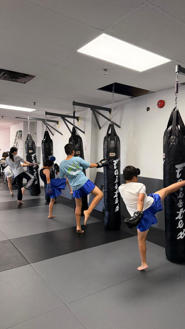 Young Muay Thai students practising kicks on heavy bags